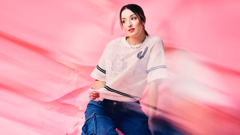 sad alex seated against a pink backdrop with translucent pink fabric moving across the foreground.